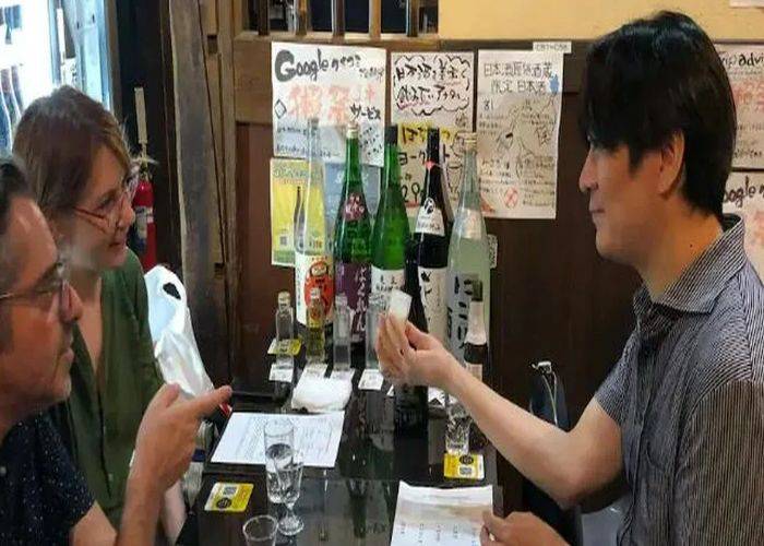 An expert guide explaining a cup of traditional Japanese sake to two guests.